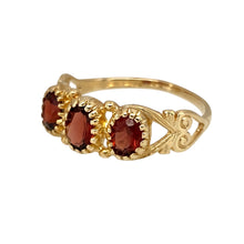 Load image into Gallery viewer, Add a touch of vintage charm to your jewellery collection with this pre-owned 9ct yellow gold &amp; garnet set trilogy ring, featuring:

Design: A classic trilogy ring, symbolising the past, present, and future, with intricate flower filigree-style shoulders for added elegance.
Material: 9-carat yellow gold, offering a warm and timeless appeal.
Gemstone: Features a 6mm by 4mm central garnet, known for its rich red hue and timeless beauty.

